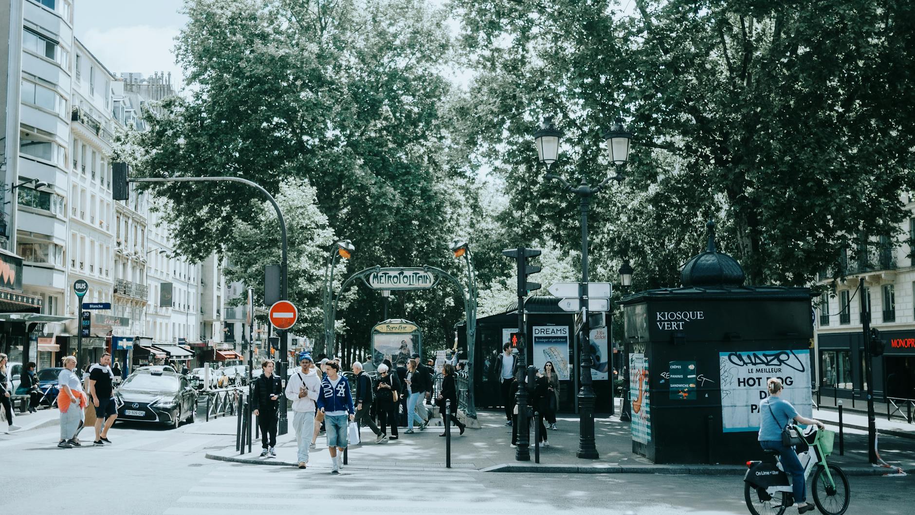 A bustling scene at a Paris metro entrance with people, trees, and signage.