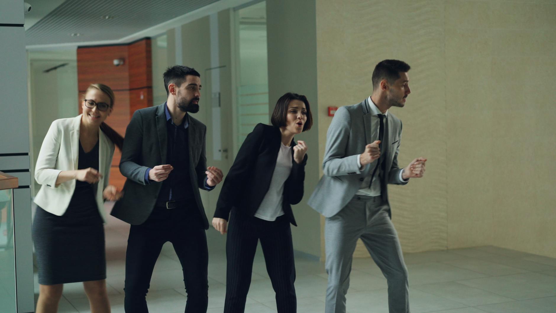 Business professionals in suits enthusiastically dance indoors, symbolizing celebration.