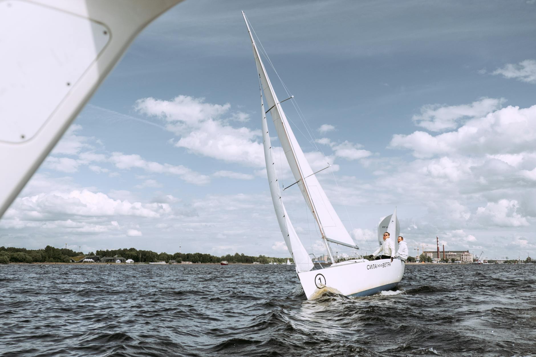 Two people navigating a sailboat on open waters under a bright sky. Ideal for adventure and travel themes.