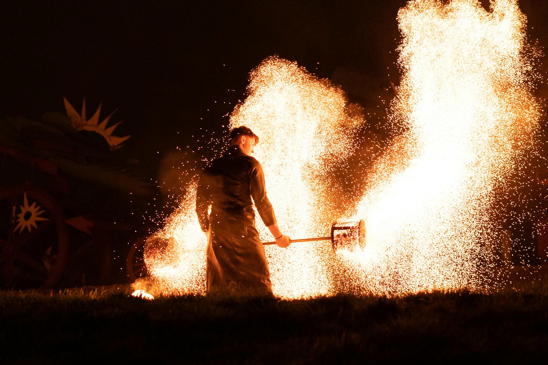 A man engaging in a dynamic fire performance, creating an intense show with sparking flames.